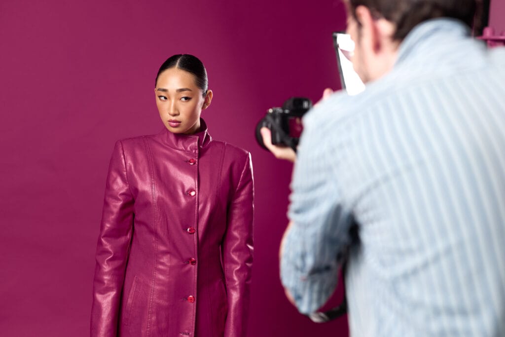 Fashionable asian brunette woman in a purple leather jacket posing for a man's photo in front of a matching purple wall